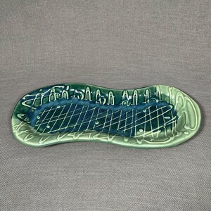 May include: A green ceramic serving dish with a wavy edge and a grid pattern in the center. The dish has a light green glaze with dark green accents.