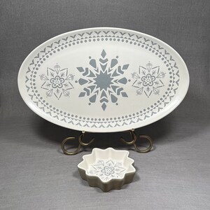 May include: A white oval serving platter with a gray snowflake design and a matching smaller white star-shaped dish. Both pieces have a gray snowflake design.