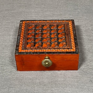 以下が含まれることがあります： 蓋に彫刻が施された木製の箱で、真鍮製のつまみがあります。箱は茶色で、濃い茶色の彫刻が施されています。