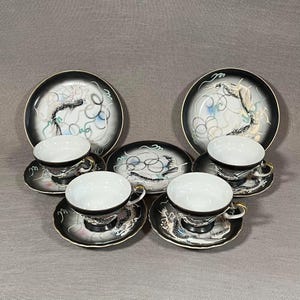 May include: A set of four black and white teacups and saucers with a dragon design. The cups and saucers have a gold trim.