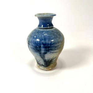 May include: A small, blue and white ceramic vase with a wide base and a narrow neck. The vase has a speckled glaze and a subtle design.
