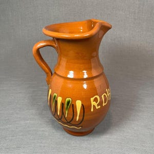 May include: A brown ceramic jug with a green and yellow floral design and the text "RDA" on the side.