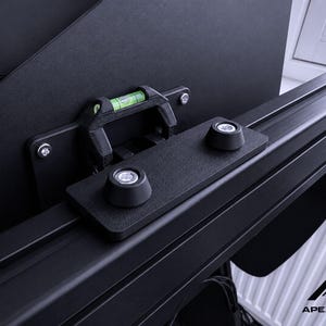 May include: Close-up of a black mounting bracket with a built-in level and two black knobs. The bracket is attached to a black rail system. The logo "APEXLAYER" is visible in the bottom right corner.