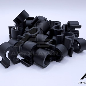 Può includere: Un mucchio di clip per cavi in plastica nera. Le clip hanno un design curvo con un elemento a forma di gancio. Il logo "APEXLAYER" è visibile in basso a destra.