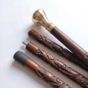 May include: A collapsible walking stick featuring a polished brass handle and a dark brown wooden shaft. The shaft is intricately carved with floral patterns and consists of three segments connected by metal screws, ending in a black rubber tip.
