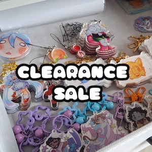 May include: A collection of colorful acrylic charms and keychains, featuring various cartoon characters and designs. The image displays a variety of shapes and sizes, including round, rectangular, and star-shaped charms. The text "CLEARANCE SALE" is prominently displayed across the image.