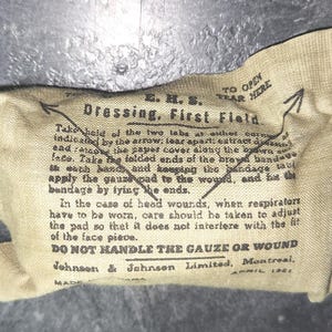 Puede incluir: Un paquete de vendaje de primeros auxilios vintage, de color beige, con texto negro y flechas que indican cómo abrirlo. El texto incluye instrucciones y el nombre del fabricante, Johnson & Johnson Limited, Montreal.