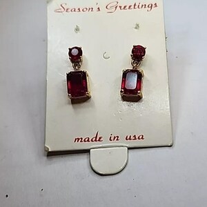 May include: A pair of red gemstone earrings with gold settings. The earrings are on a white card with the text "Season's Greetings" and "made in usa".