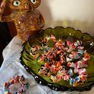May include: A bowl filled with colorful scrunchies in a variety of floral and abstract patterns. The scrunchies are made of soft fabric and are perfect for adding a pop of color to any outfit.