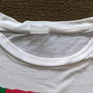 K&ouml;nnte beinhalten: Wei&szlig;es T-Shirt mit einem wei&szlig;en Etikett, das in den Nacken eingen&auml;ht ist.