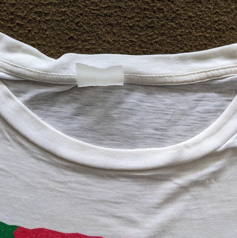 K&ouml;nnte beinhalten: Wei&szlig;es T-Shirt mit einem wei&szlig;en Etikett, das in den Nacken eingen&auml;ht ist.