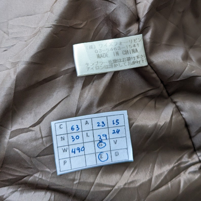 May include: A white tag with black text that reads "(株)ワイズフォーリピン 03-5463-1541 MADE IN CHINA タンブラー乾燥はお避け下さい アイロンは浮かしておかけ下さい" and a white tag with a grid of numbers and letters. The numbers on the tag are 63, 30, 490, 23, 15, 39, 24.