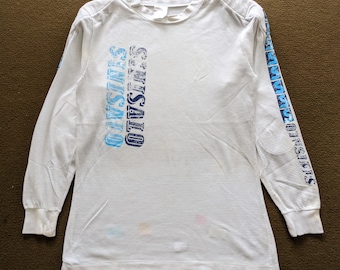 May include: White long-sleeved thermal shirt with blue and white text that reads "OUTSIDERS" on the front and "OUTSIDERS" on the sleeve.