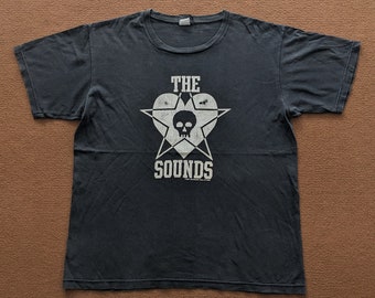 May include: Black t-shirt with a white graphic of a skull inside a heart with a star. The text "THE SOUNDS" is below the graphic.