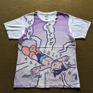 Puede incluir: Camiseta blanca con un estampado gráfico morado y blanco de Mighty Atom volando por el aire con estrellas y rayos. El texto "Mighty Atom" está impreso en la parte inferior de la camiseta. El texto japonés "ビビビ" está impreso en la camiseta.