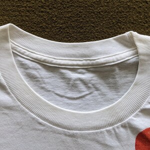 May include: Close-up of the neckline of a white t-shirt. The neckline is a crew neck and has a ribbed texture.
