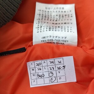 May include: Close-up of a white tag with black text that reads "(株)フラッグシップ TEL:048-762-1021 MADE IN CHINA". Below the tag is a white tag with black text and numbers. The tag reads "C 210 A 24 21 N 16 L 27 26-5 W 840 E V D P".