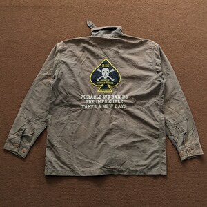 May include: A green long-sleeved shirt with a black spade and skull patch that says "Mobile Strike Force Commando" and the text "Miracle we can do the impossible takes a new days".