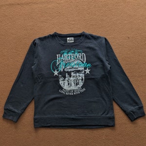 May include: A dark blue long-sleeved sweatshirt with a graphic print of a crest featuring the text "HARTFORD FreeStone 1856-1900 SAINT OF SPIRIT LONG RIVER WITH TIDE".