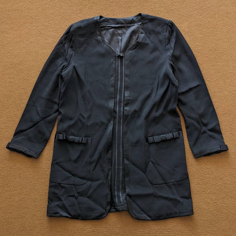 May include: A black long-sleeved jacket with a zipper closure and two pockets with decorative ruffles. The jacket has a v-neck and a satin lining.