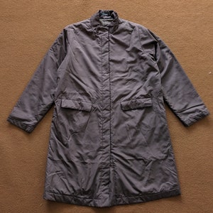 May include: A long, dark gray, quilted coat with a stand-up collar and a zipper closure. The coat has two large pockets on the front.