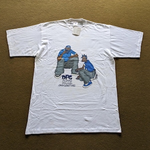 May include: White t-shirt with a graphic print of two cartoon figures. The figures are wearing blue and white clothing. The text "DPG" is printed below the figures, with the words "Puppy Pound Gangstaz" printed below that.