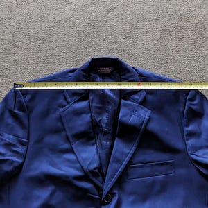 Puede incluir: Un blazer azul marino con cierre de un solo bot&oacute;n y solapa con muescas. El blazer se mide con una cinta m&eacute;trica. La etiqueta dice "MADE IN USA". El ancho total del blazer es de aproximadamente 45,7 cm.