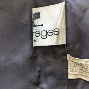 May include: A white label with black text that reads "reges" and "ris" in a cursive font. The label is attached to a black fabric.