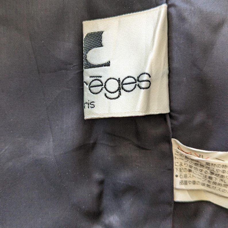 May include: A white label with black text that reads "reges" and "ris" in a cursive font. The label is attached to a black fabric.