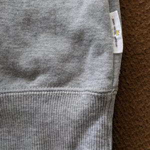 Puede incluir: Sudadera gris con dobladillo de canal&eacute; y una peque&ntilde;a etiqueta blanca con el texto "JEAN-MICHEL BASQUIAT" y un gr&aacute;fico de corona.