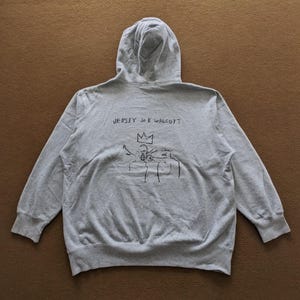 Puede incluir: Sudadera con capucha gris con un estampado gr&aacute;fico negro de una persona con una corona y otras dos personas. El texto "JERSEY JOE WALCOTT" est&aacute; impreso sobre el gr&aacute;fico.