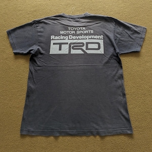 May include: A dark gray t-shirt with a white graphic print on the back. The graphic says "Toyota Motor Sports Racing Development TRD".