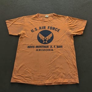 May include: Orange t-shirt with a blue U.S. Air Force logo and the text "Davis-Monthan A.F. Base Arizona".