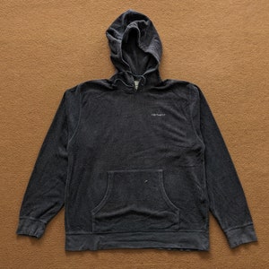 Op de afbeelding: Een donkergrijze hoodie met een voorzak en het woord "Carhartt" geborduurd op de borst.