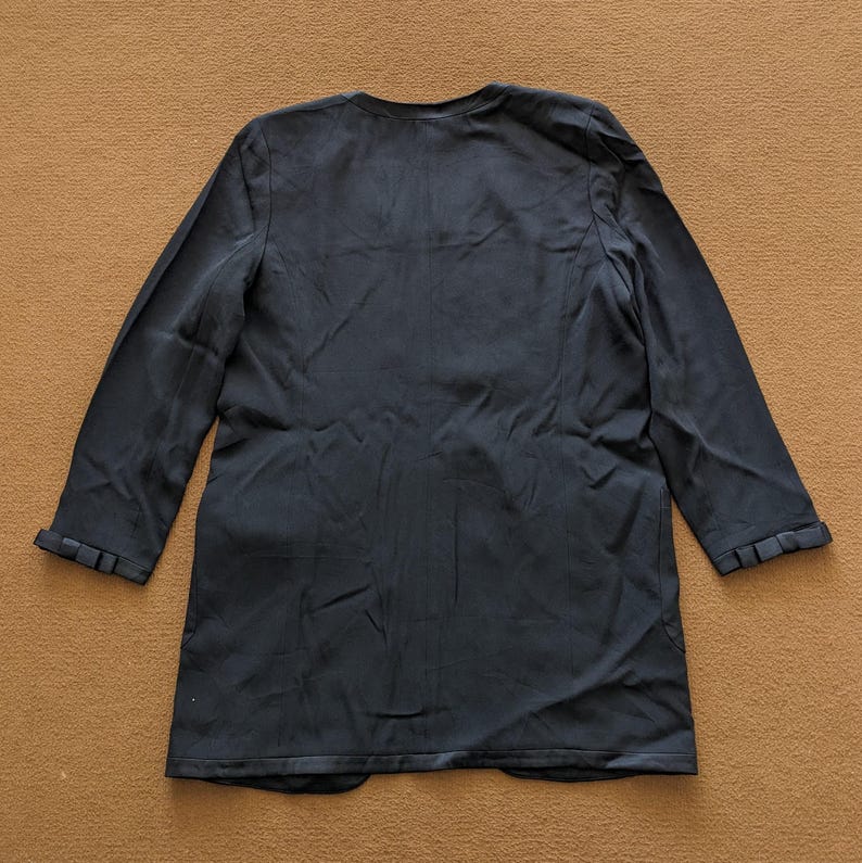 May include: A black long-sleeved blazer with a v-neck and a slightly flared hem.