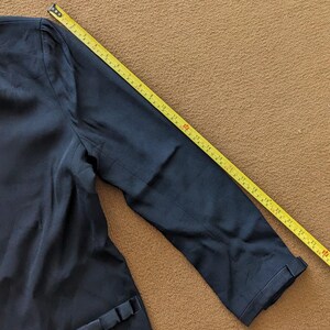 May include: A dark blue blazer with a long sleeve. The sleeve is folded up and a measuring tape is visible.
