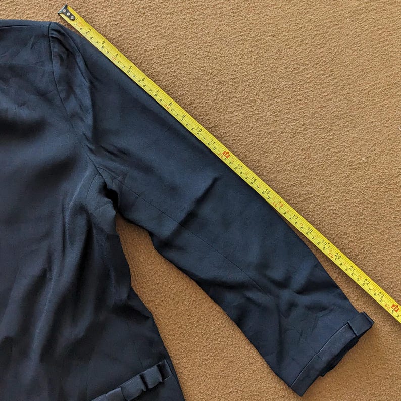 May include: A dark blue blazer with a long sleeve. The sleeve is folded up and a measuring tape is visible.
