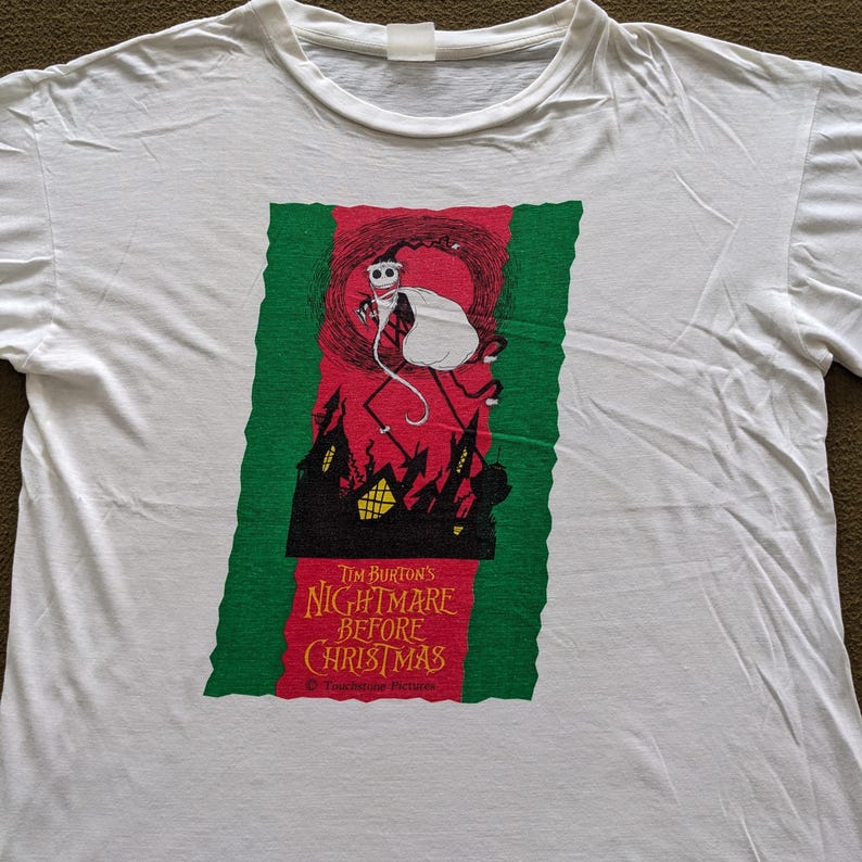 K&ouml;nnte beinhalten: Wei&szlig;es T-Shirt mit einem gr&uuml;nen, roten und schwarzen Grafikdruck von Jack Skellington aus dem Film "Nightmare Before Christmas". Der Text "Tim Burton's Nightmare Before Christmas" ist unter dem Grafikdruck gedruckt.