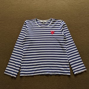 May include: A blue and white striped long-sleeve shirt with a red heart logo on the left side. The logo has a white outline and two black eyes.