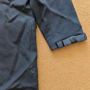 May include: A dark blue blazer with a long sleeve and a decorative detail on the cuff. The blazer has a pocket on the left side.