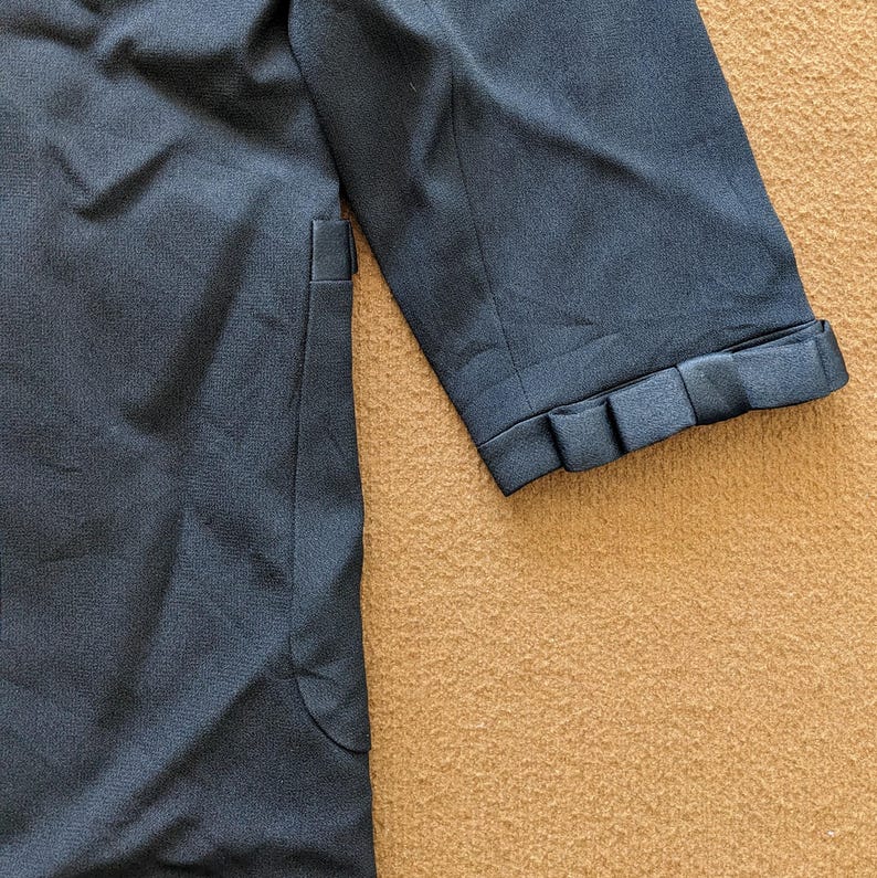 May include: A dark blue blazer with a long sleeve and a decorative detail on the cuff. The blazer has a pocket on the left side.