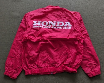 May include: A red Honda Grand Prix Racing Team jacket. The jacket has a white Honda logo and text on the back. It features a zipper closure and long sleeves. The jacket is made of a lightweight material.