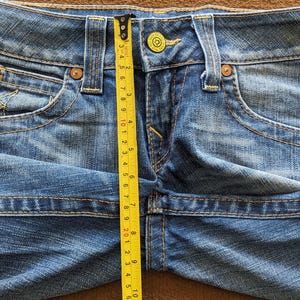 May include: A close-up of a pair of blue denim shorts with a yellow measuring tape. The tape measures 10 inches.