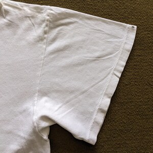 May include: Close-up of the white cotton sleeve of a t-shirt. The sleeve is folded over and the stitching is visible.