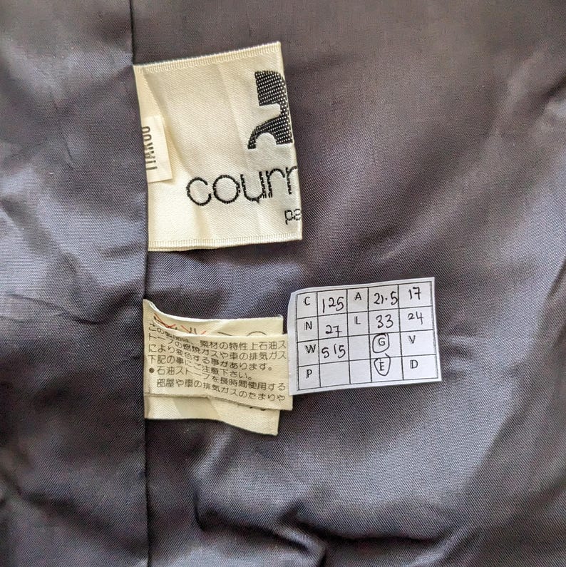 May include: A white tag with the word "courn" printed in black. A second tag with a size chart in black and white text. The chart includes the letters C, N, W, P, A, L, 21-5, 17, 33, 24, G, V, E, and D.