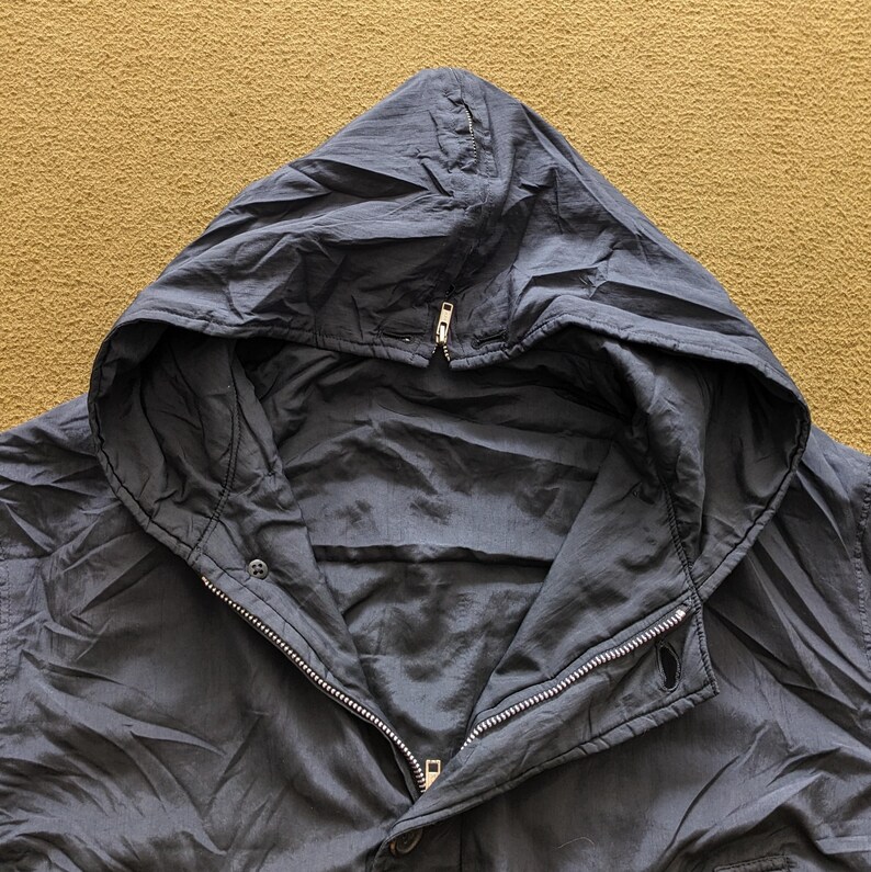 Puede incluir: Chaqueta con capucha azul marino oscuro con cierre de cremallera y botones a presi&oacute;n. La chaqueta tiene una capucha con cord&oacute;n y una tela ligera y ligeramente brillante. Prenda de vestir exterior informal.