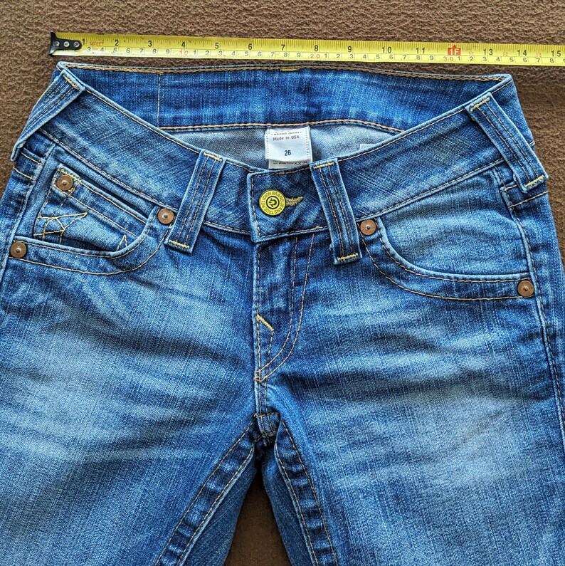 May include: A pair of blue denim jeans with a yellow button and stitching. The jeans have a low rise and a straight leg.