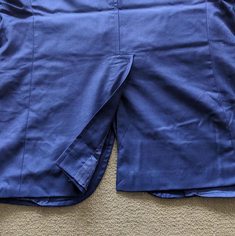 Puede incluir: Primer plano de una blazer azul marino, mostrando la textura de la tela y la abertura trasera. La prenda est&aacute; hecha de un material liso, con costuras visibles y un dise&ntilde;o elegante.