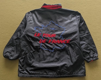 May include: Black jacket with red trim featuring the words "LE TOUR DE FRANCE" in red, and a blue outline of France. The jacket has a collar and long sleeves. The text "O PARIS" is above the map outline.