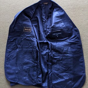 Puede incluir: Blazer azul marino abierto, que revela el forro interior y los bolsillos. El blazer tiene etiquetas que dicen "Southwick" y "Comme des Garcons". El forro es de un tono azul m&aacute;s oscuro que la tela exterior.